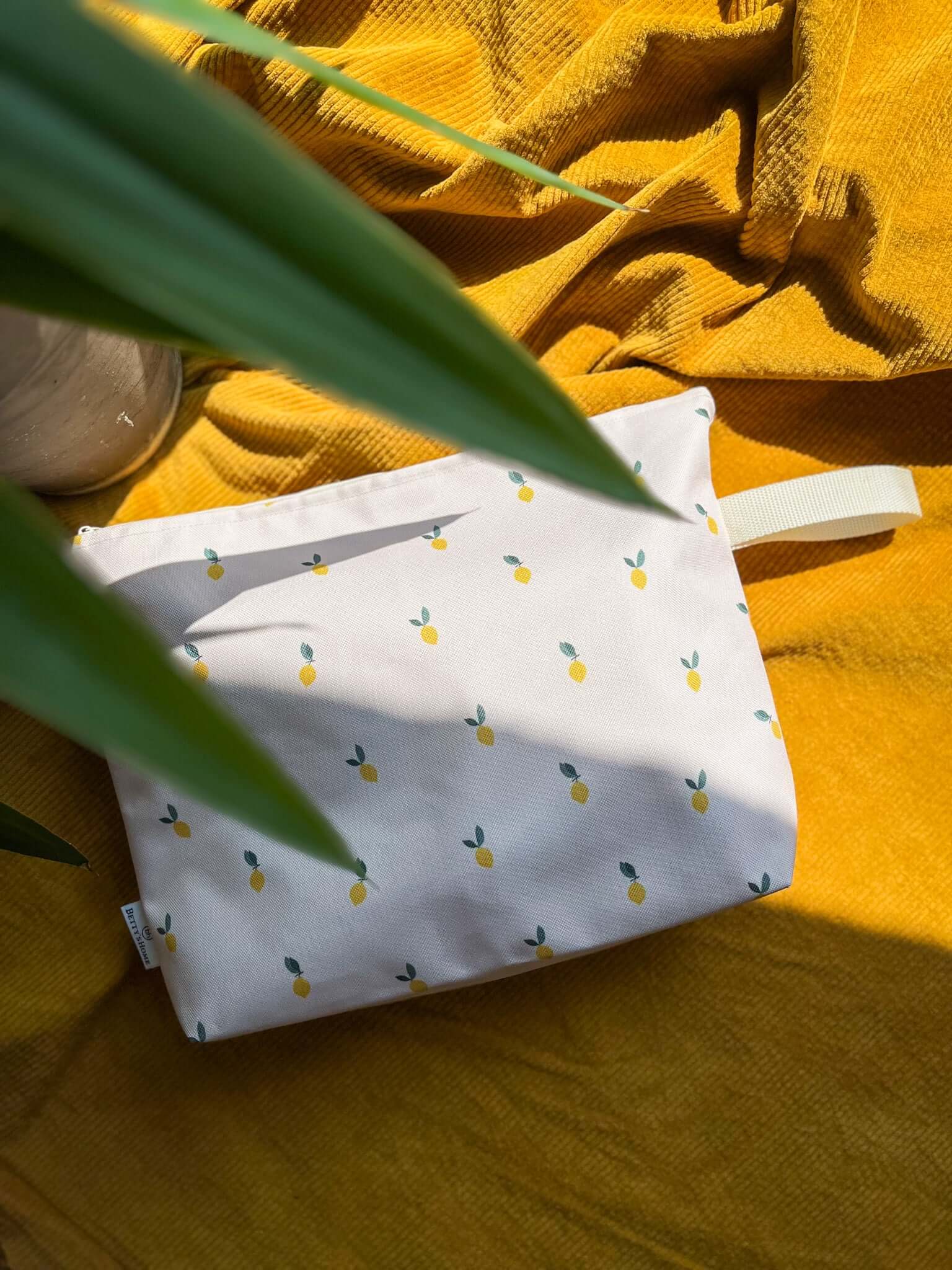 A cosmetic bag in lemons in which you can store your most important items while traveling. The cosmetic bag sits on a mat on the beach. Cosmetic bags from Bettys Home 