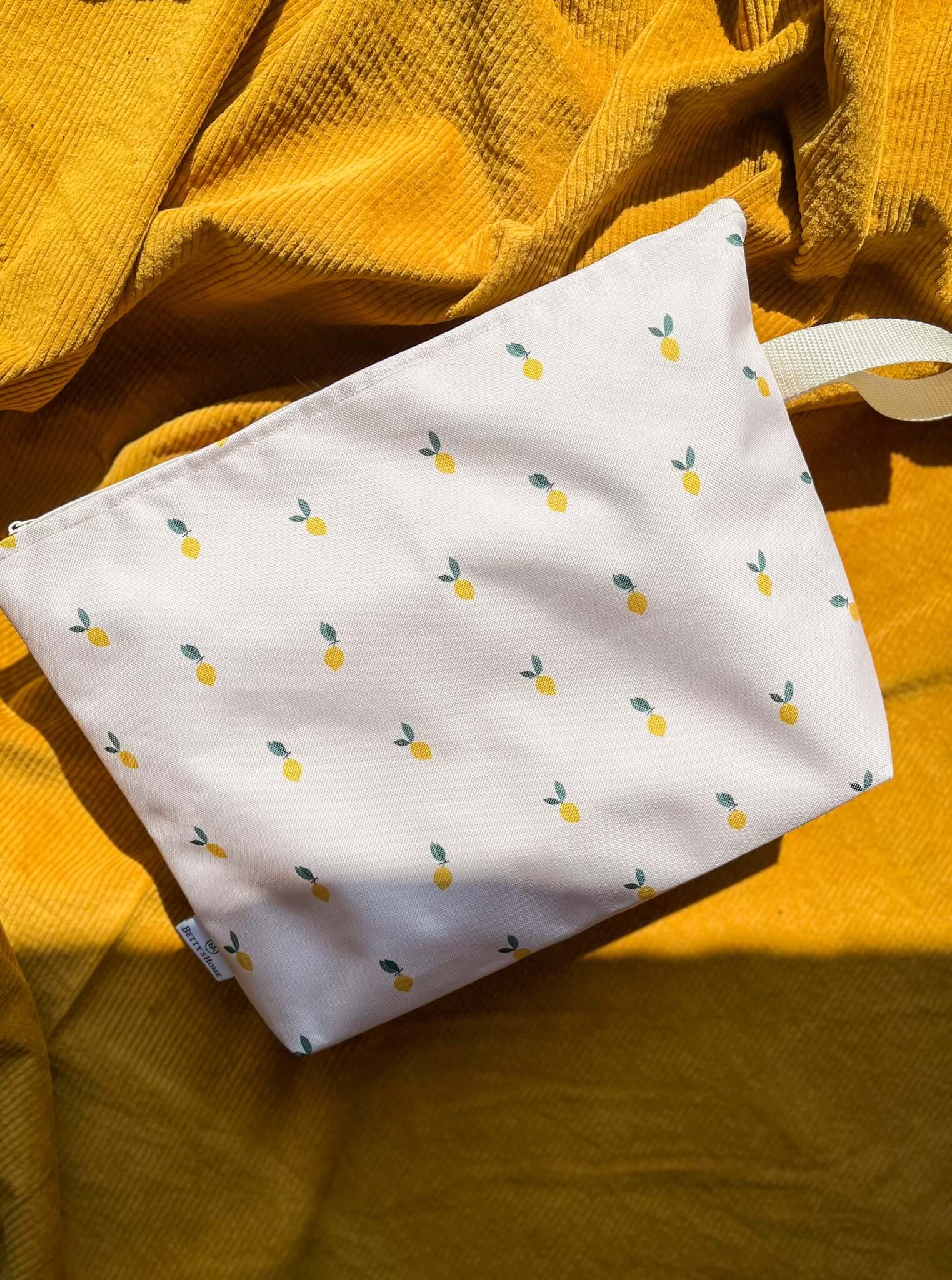 Beach cosmetic bag with a pattern of lemons lies on a mat on the beach. The cosmetic bag contains the most necessary items for summer vacation from Bettys Home