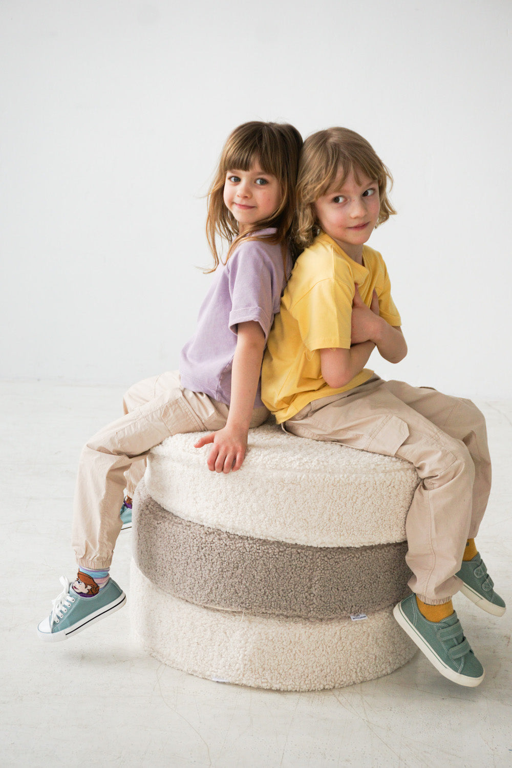 little kids sitting on large boucle pouf by bettys home. both smiling  