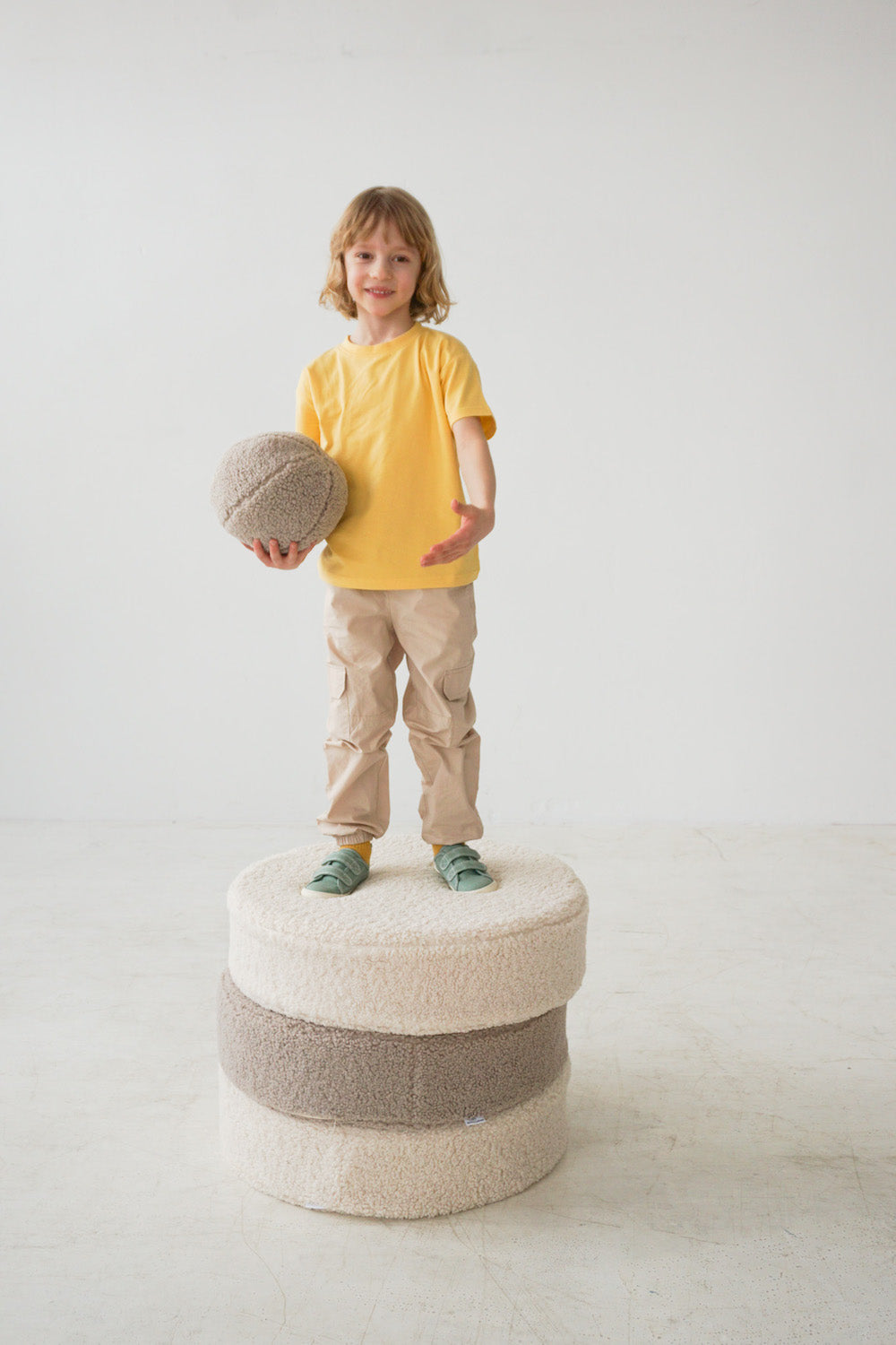 a boy standing on large boucle poufs and keeps boucle ball by bettys home in hands 