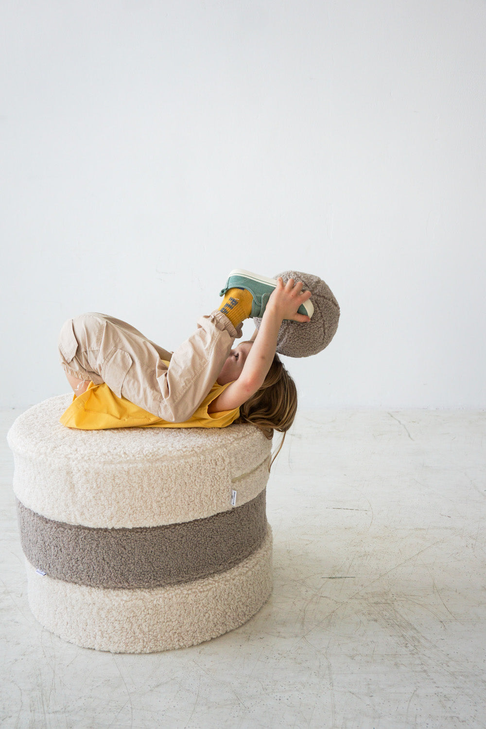 little boy playing on boucle pouf with boucle ball by bettys home in his hands