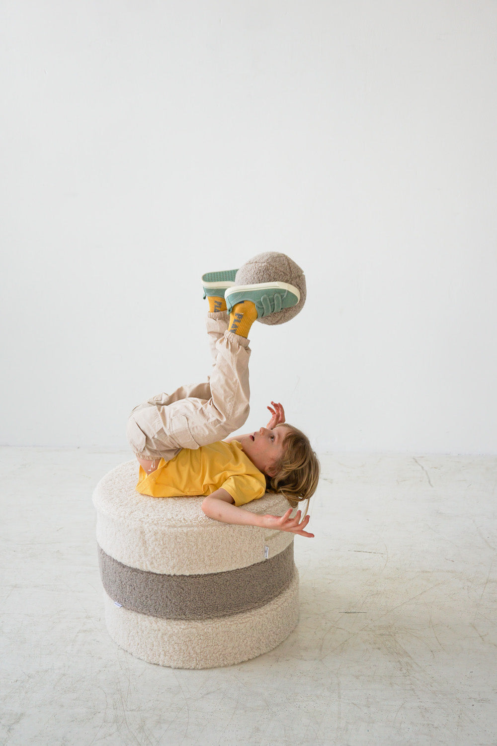 little boy playing on boucle pouf with boucle ball by bettys home in his legs