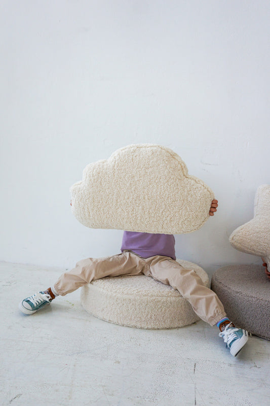 kid sitting on large boucle pouf with boucle cloud cushion by bettys home in hands.