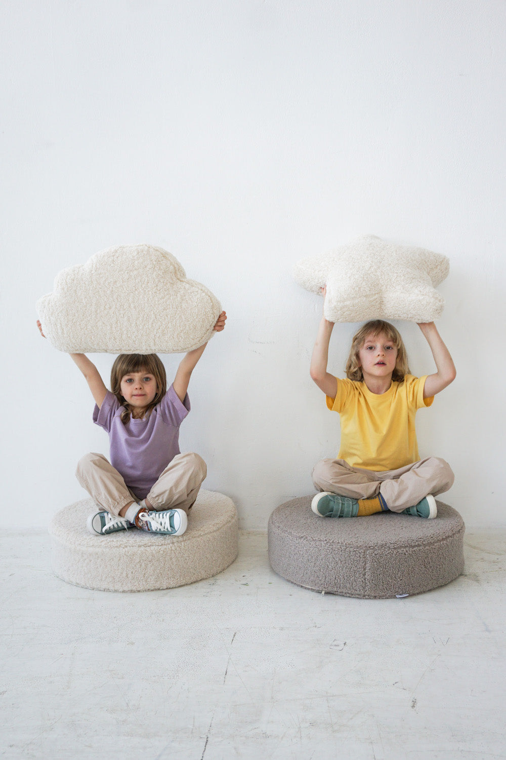 kids sitting on boucle floor poufs by bettys home with boucle cloud cushion and boucle star cushion in hands