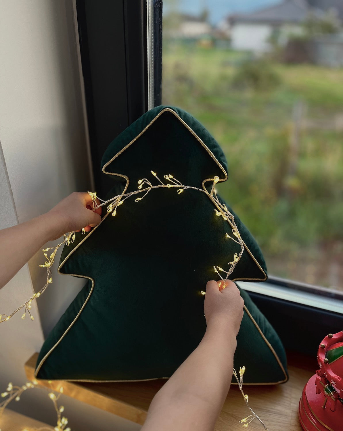 Christmas tree pillow in green velvet by bettys home standing on window and it is decorated with Christmas lights 