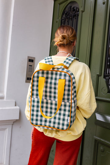 Woman with green gingham backpack by Bettys home standing in front of green door. Green Checkered backpack 