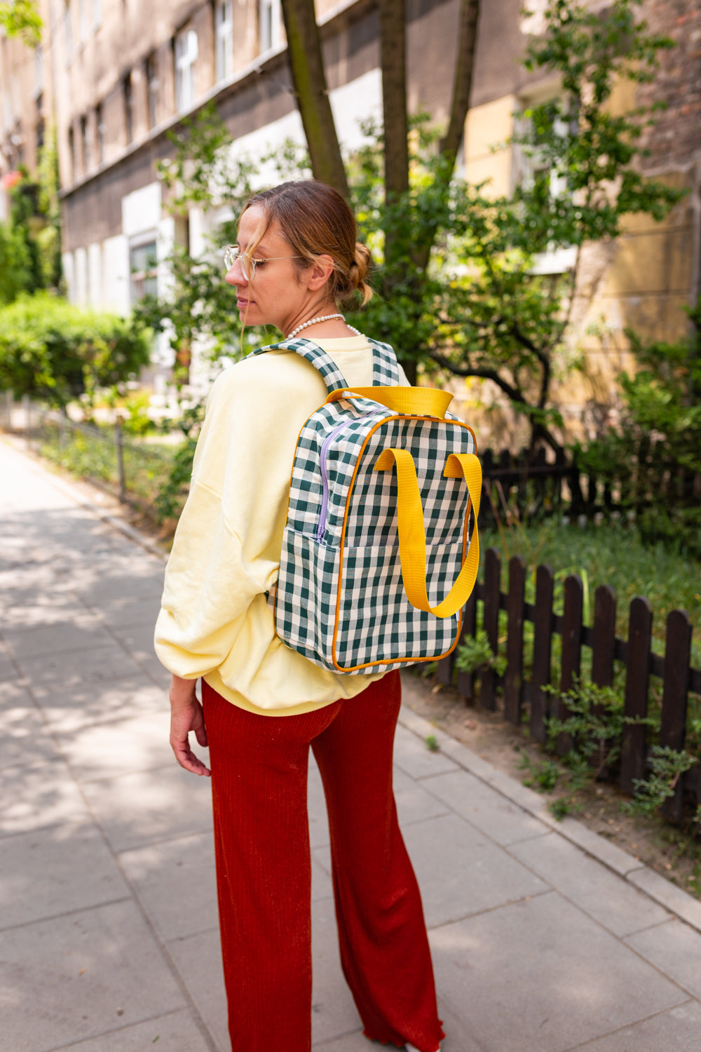 young woman in yellow blouse and red pants with green checkered backpack by bettys home on her walk 