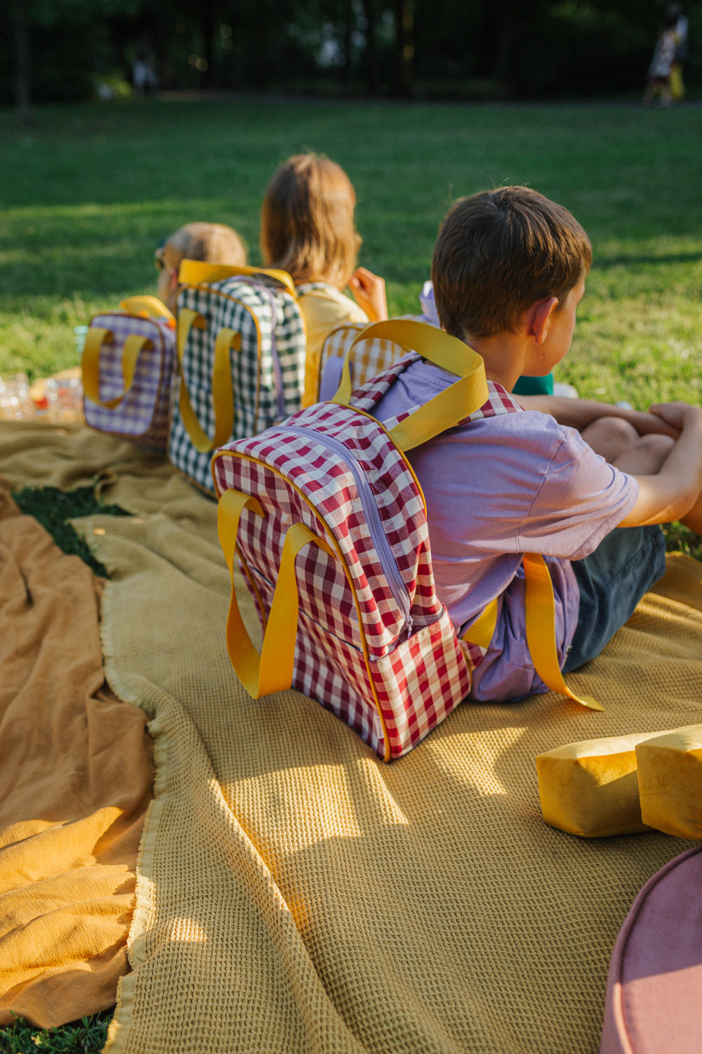 kids sitting in park on yellow blanket with gingham retro backpacks by bettys home