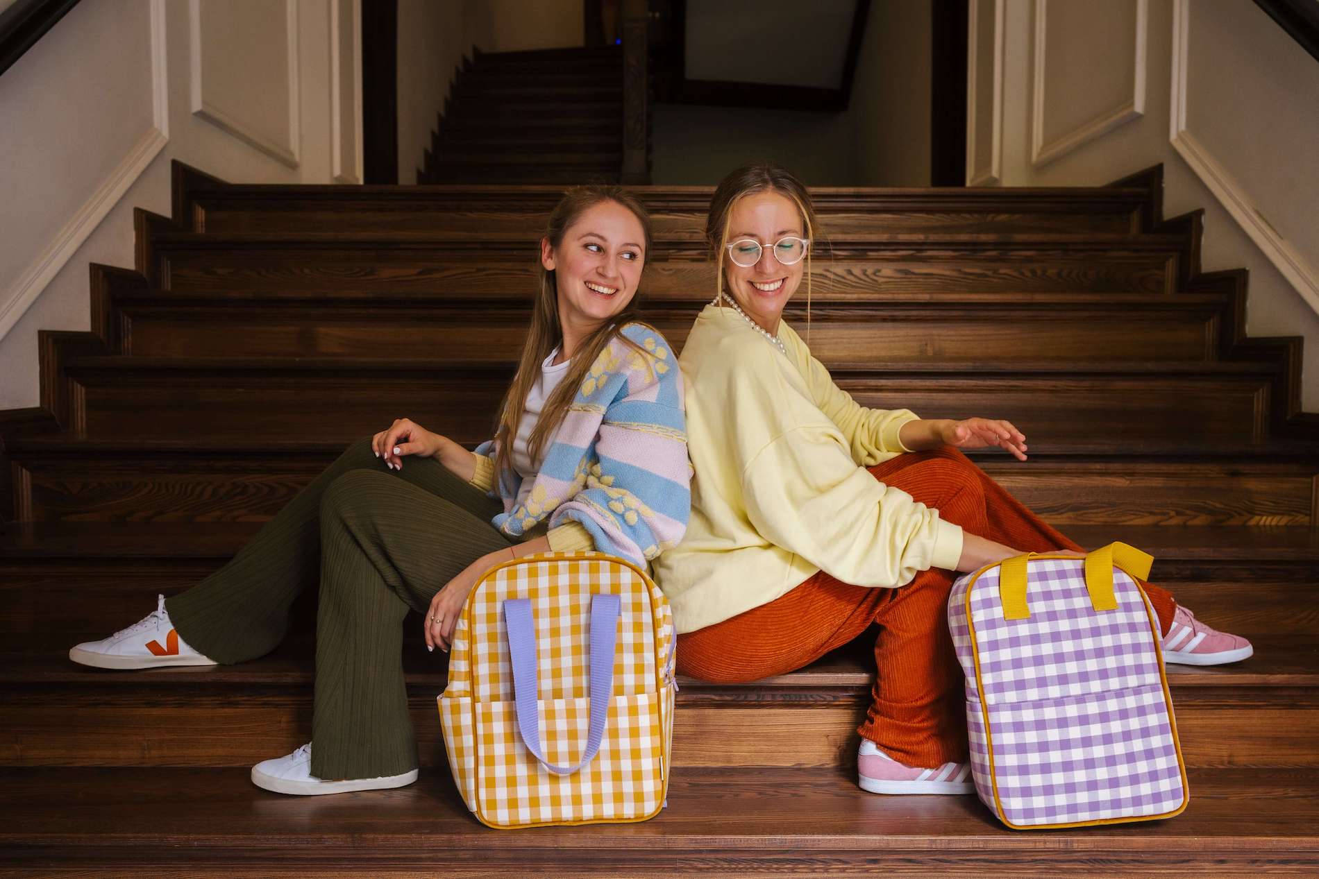 two smiling girls sitting on stars with a purple checkered backpack and yellow backpack by bettys home. Gingham backpack