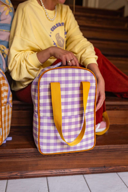 young woman in yellow blouse sitting on stairs with gingham backpack lilac by bettys home in front of her checkered backpack
