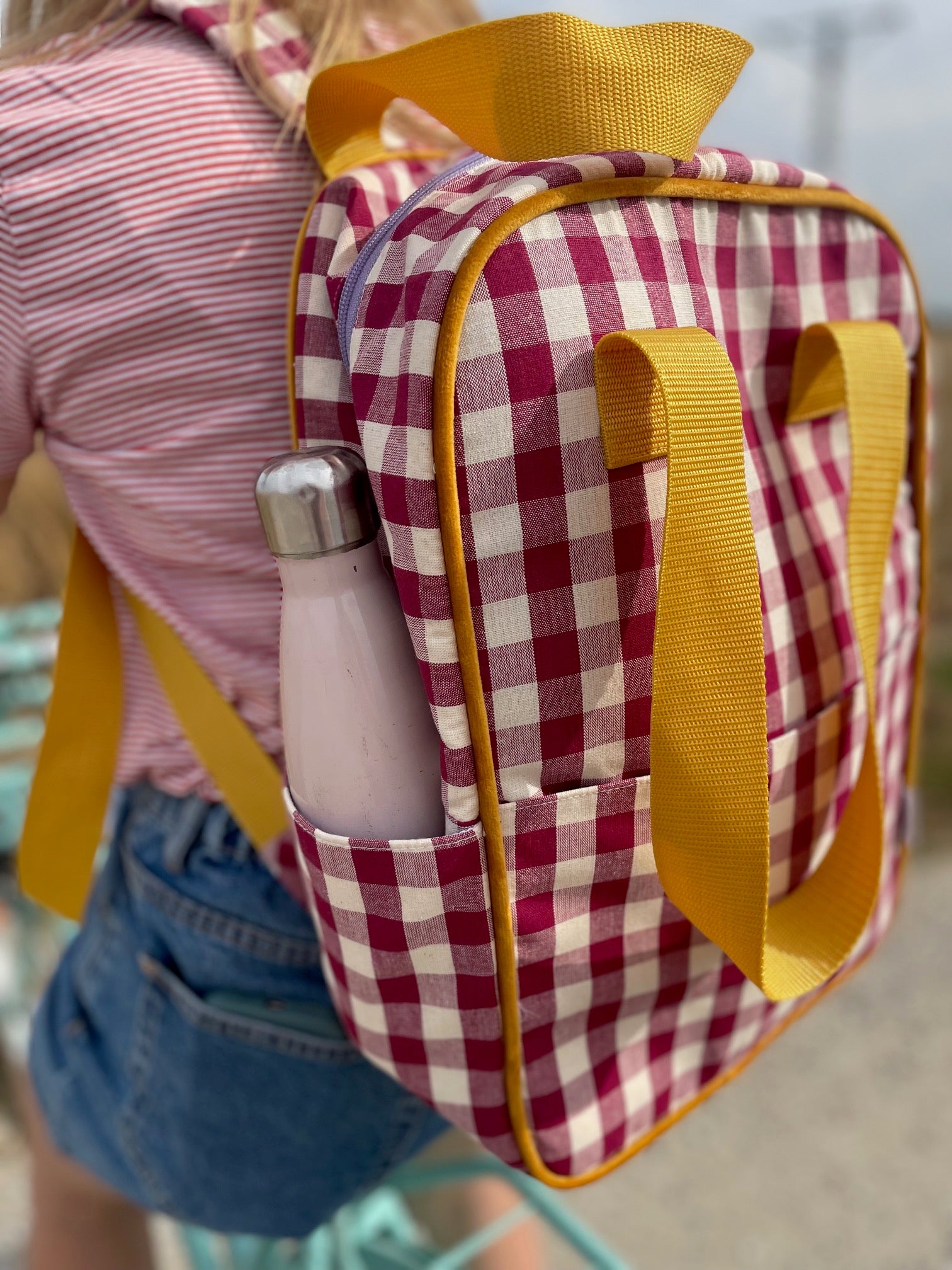 red gingham backpack by bettys home wearing by girl on bike during her trip. red checkered backpack