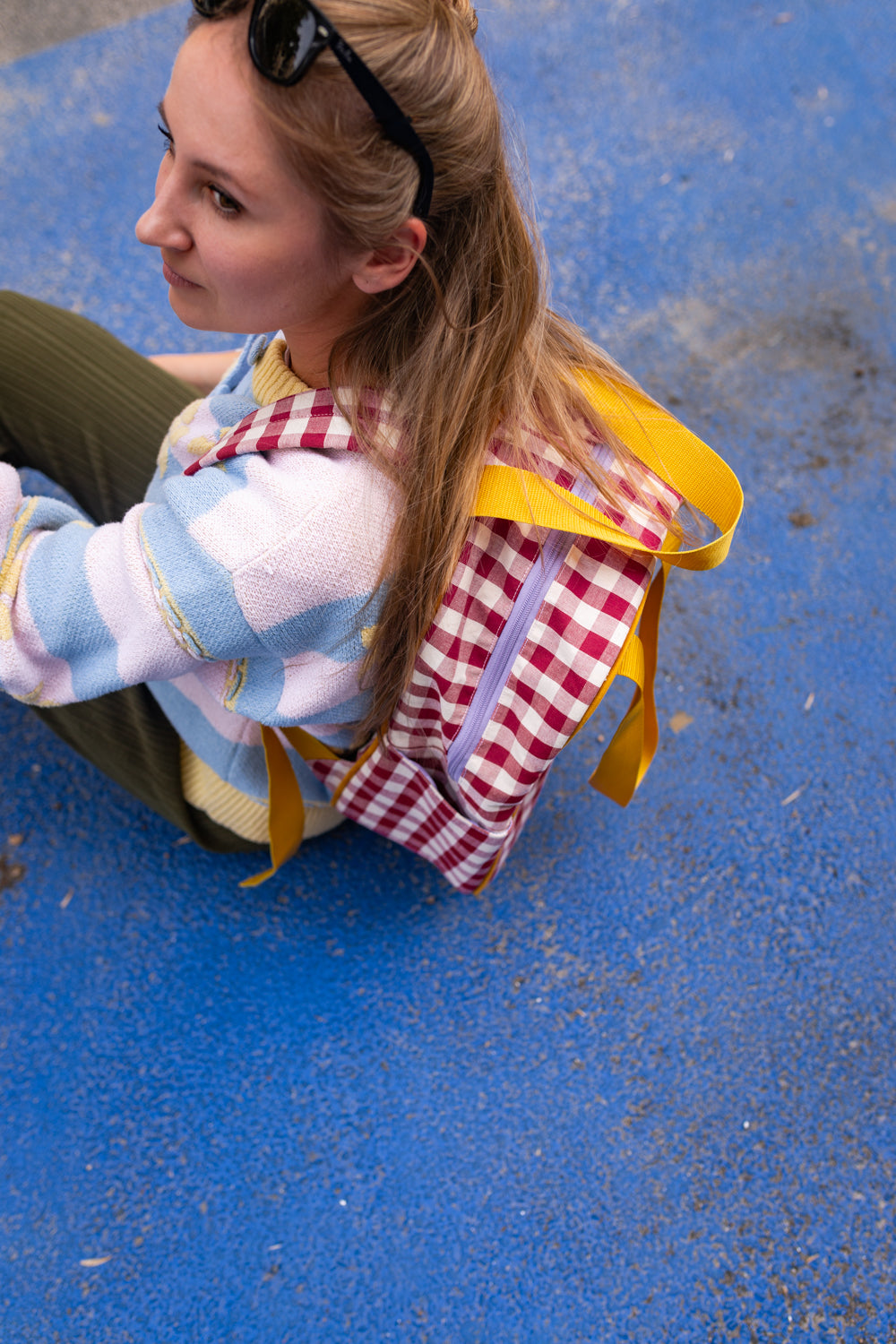 woman sitting on blue floor with red gingham backpack by bettys home. checkered backpack 