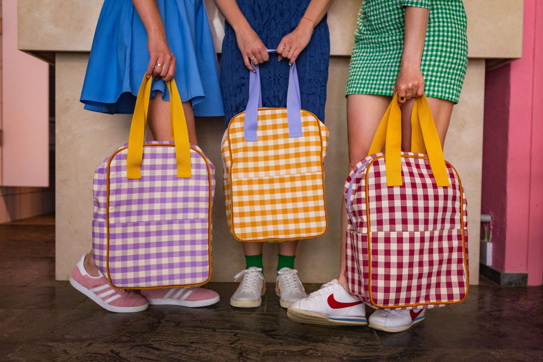 three girls colorfully dressed in restaurant with gingham backpacks by bettys home in hand. checkered city backpacks