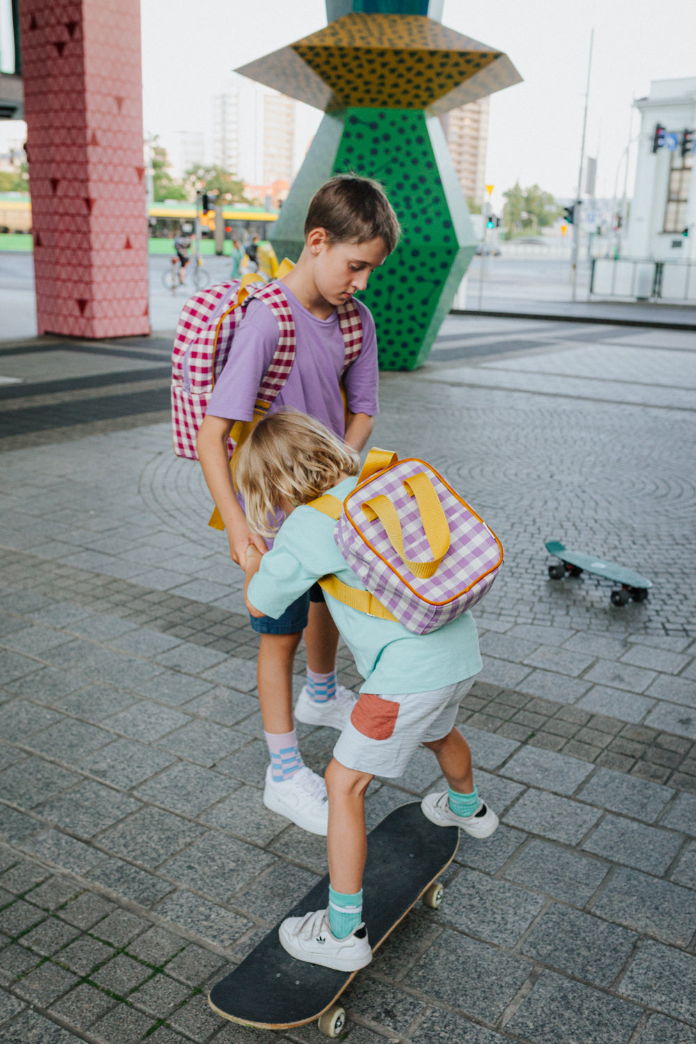 Two little boys on a skateboard while playing with a gingham backpack by bettys home. Checkered small backpack for kids