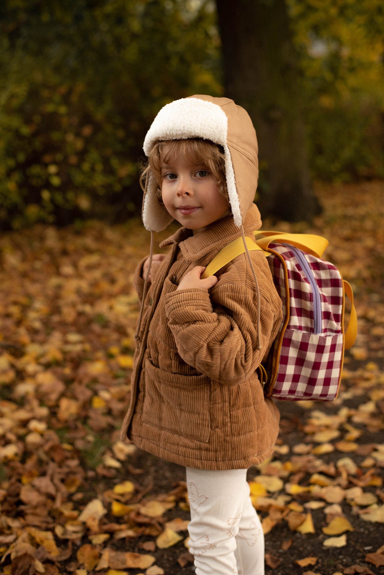 cute boy in park in autumn time with small checkered backpack by bettys home. school backpack 