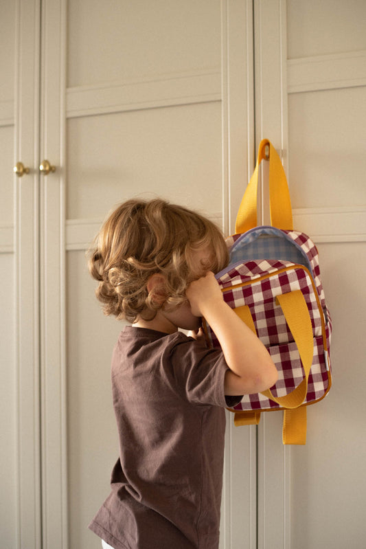 little boy peeks into little gingham backpack by bettys home. Red checkered backpack 
