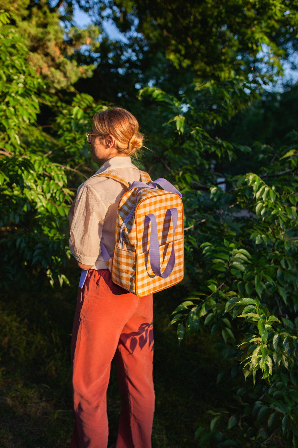 young mom during a walk in the woods has a yellow checkered backpack on her back. Gingham backpack yellow