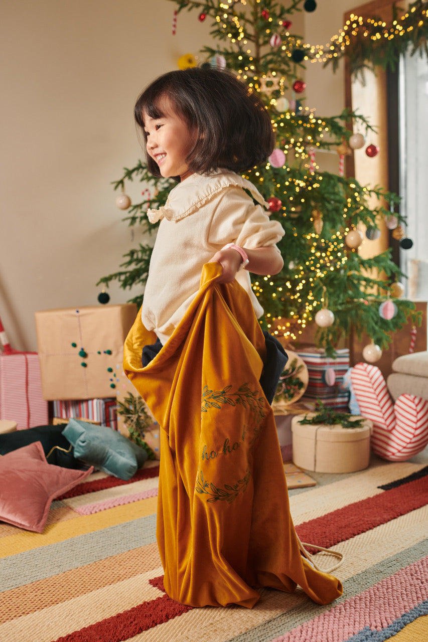 Little girl with yellow christmas bag next to Christmas tree with gifts