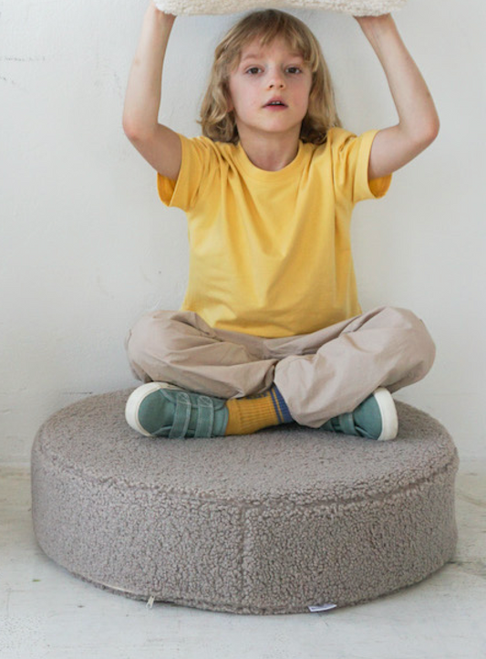 a boby in yellow t-shirt sitting on large boucle pouf in taupe bay bettys home.  