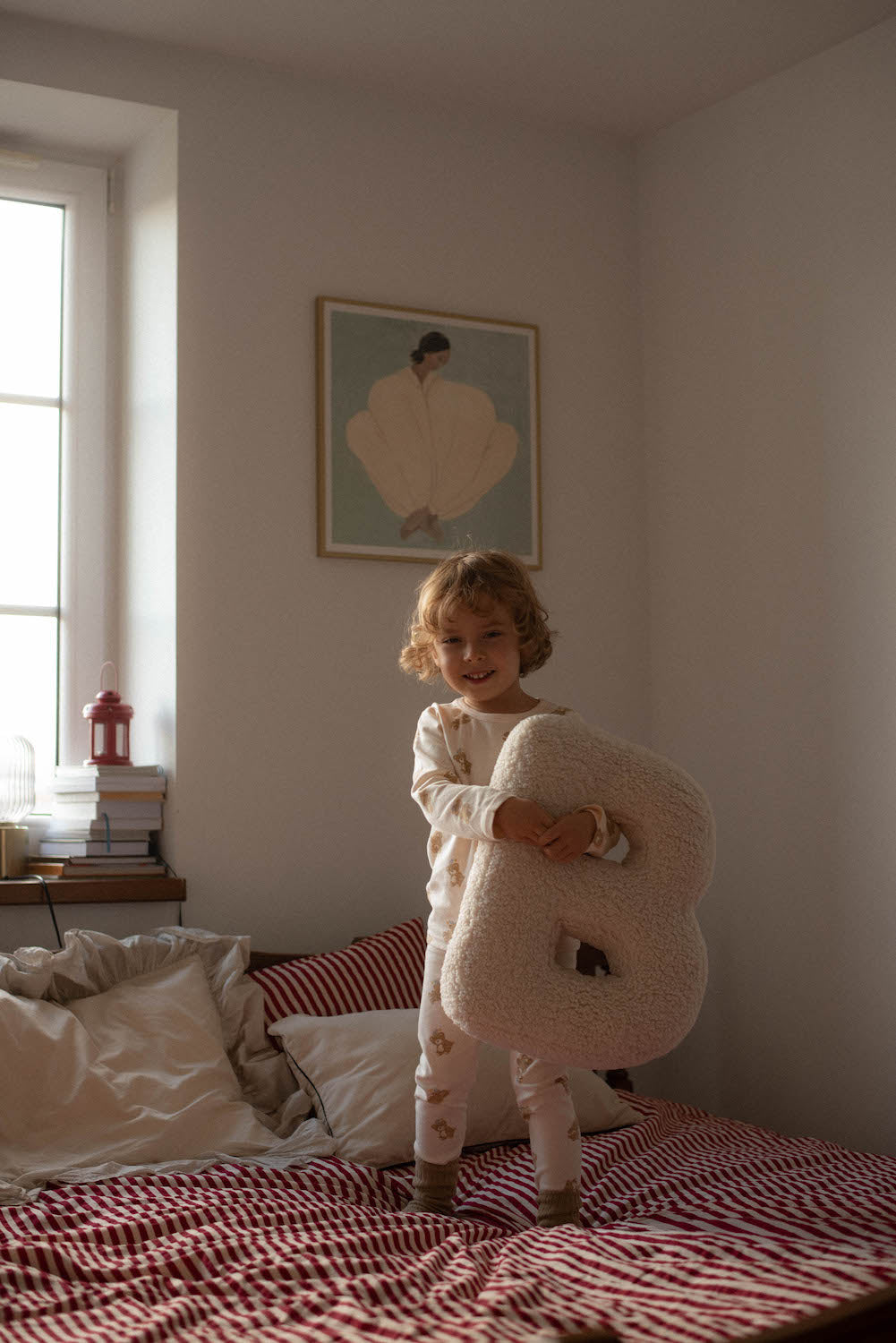 cute little boy standing on bed with boucle letter cushion N teddy pillow by bettys home in his hands