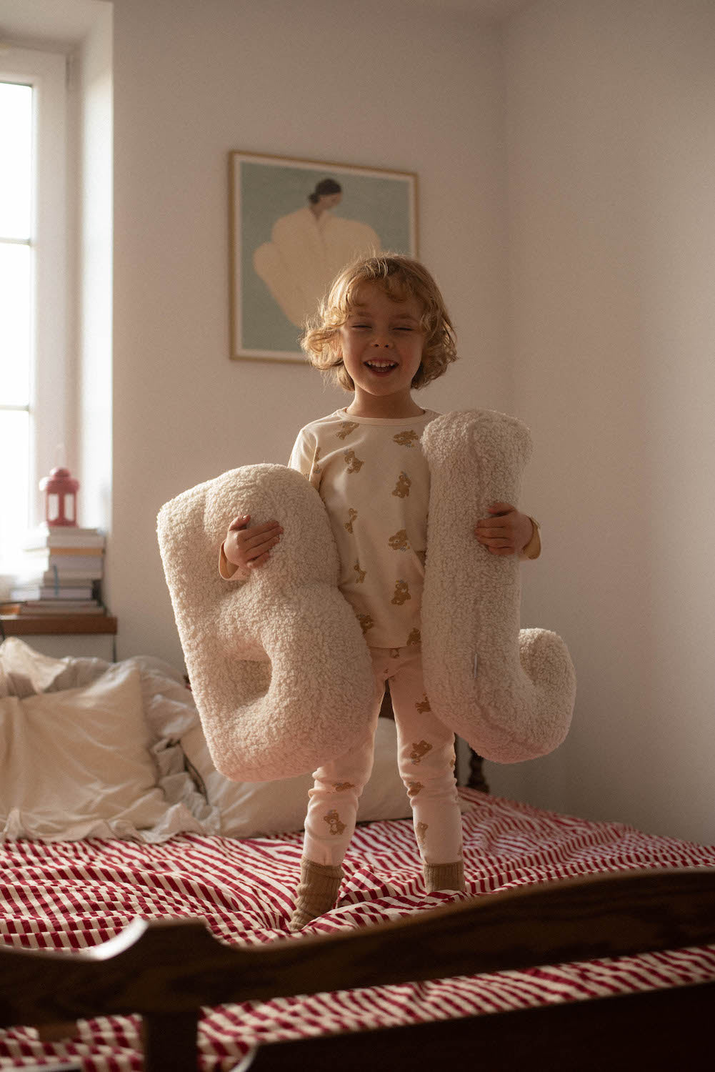 cute little boy standing on bed and holding boucle letter cushion by bettys home in his hands 