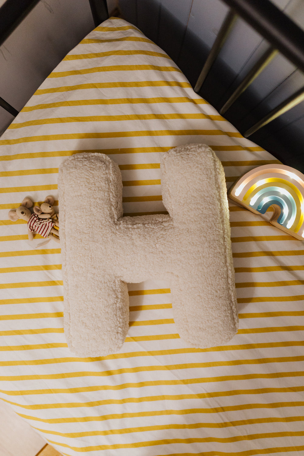 Boucle Letter cushion H by Bettys Home Teddy Letter Pillow lying in child crib on yellow stripe sheet