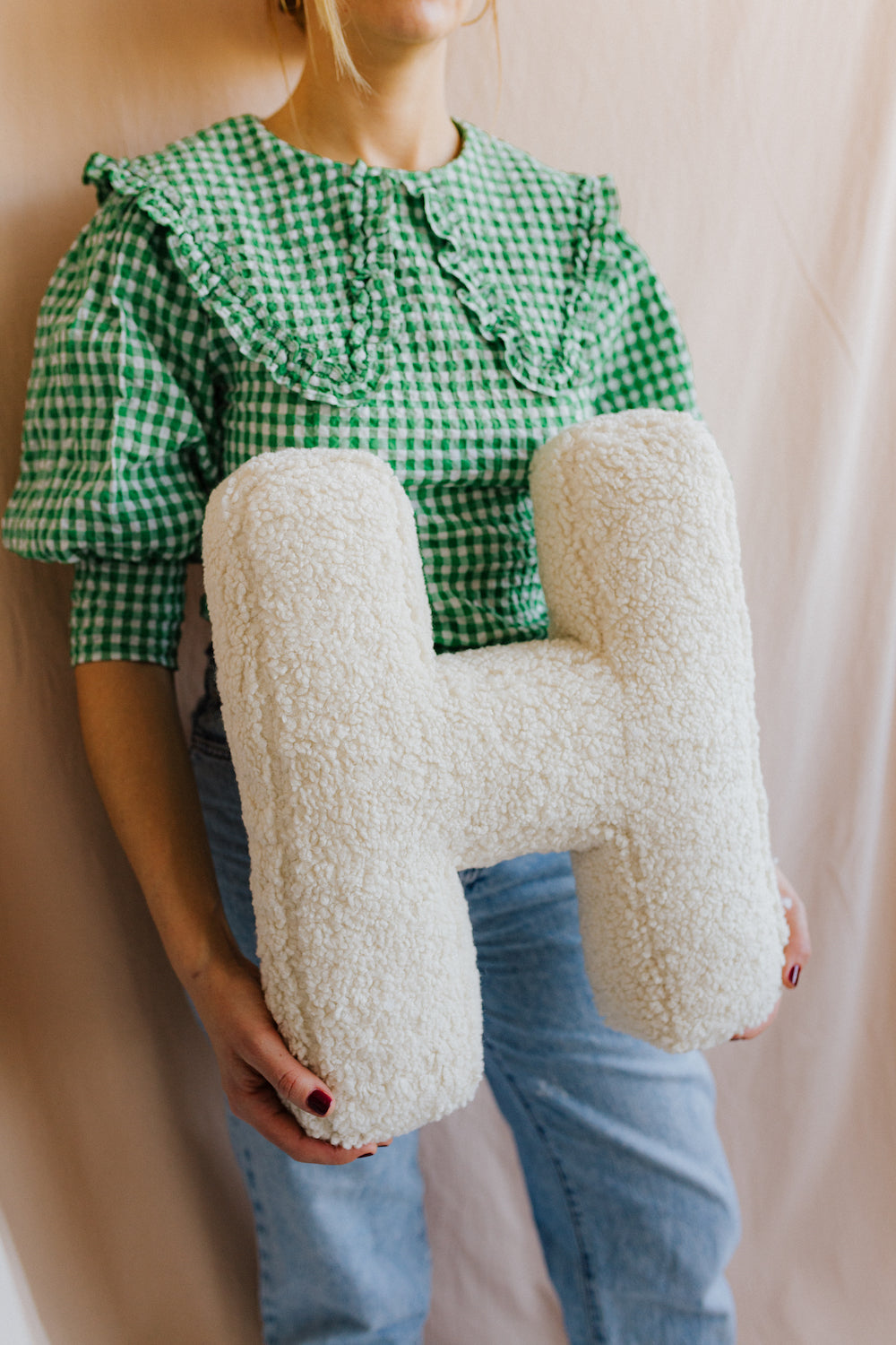 boucle letter cushion H teddy pillow by bettys home held by woman in green shirt on cream background