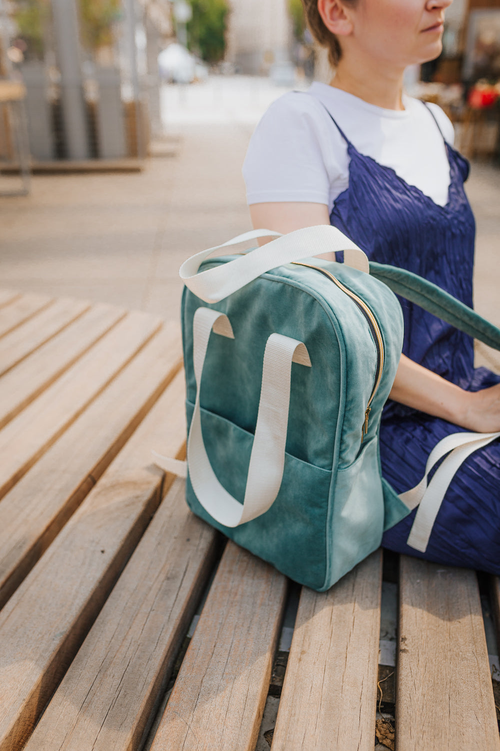 woman sitting on wooden terrace next to velvet backpack in mint. ladies backpack for travel 