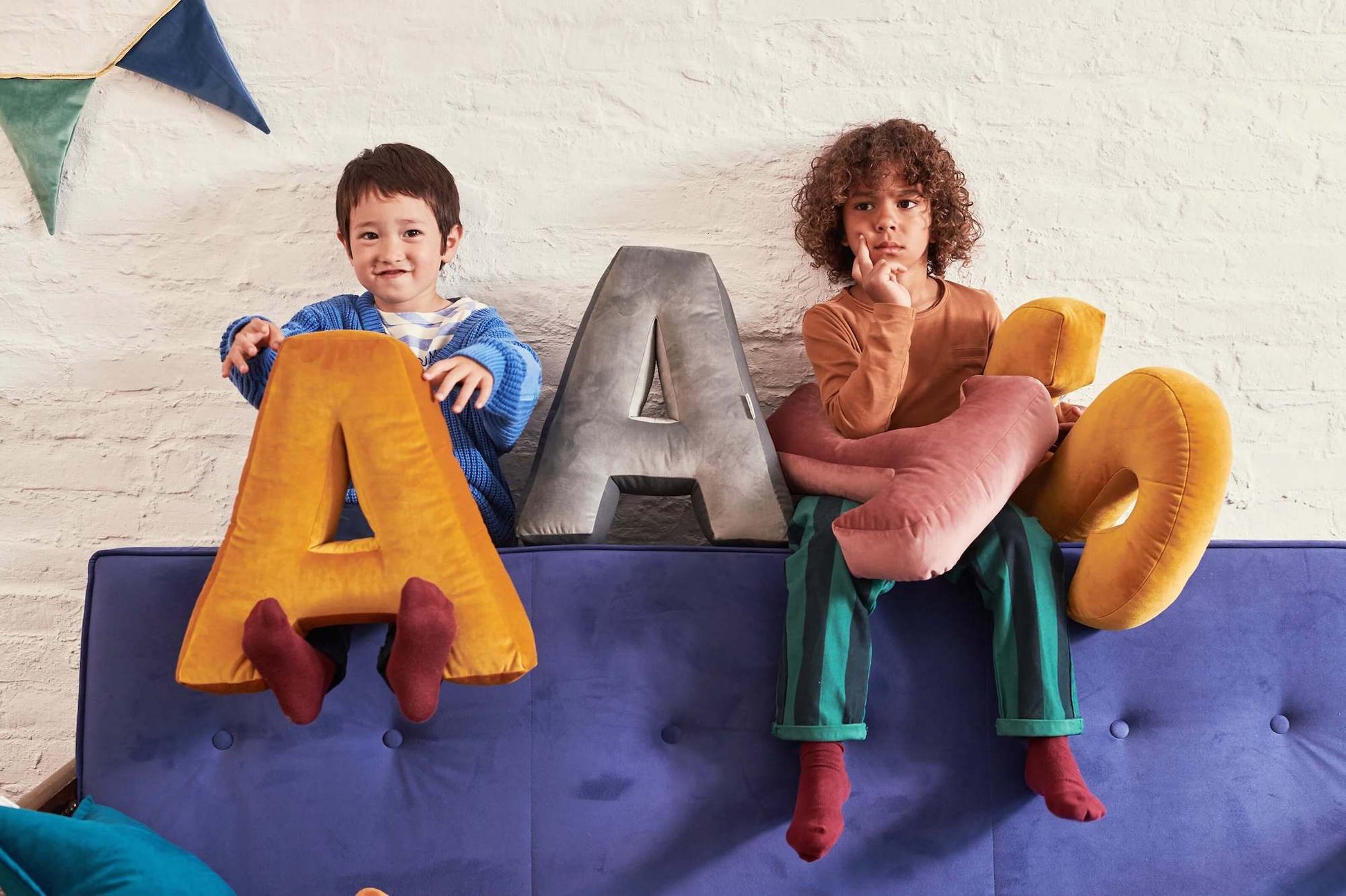 two boys sitting on couch with Velvet letter cushions by Bettys Home in hands