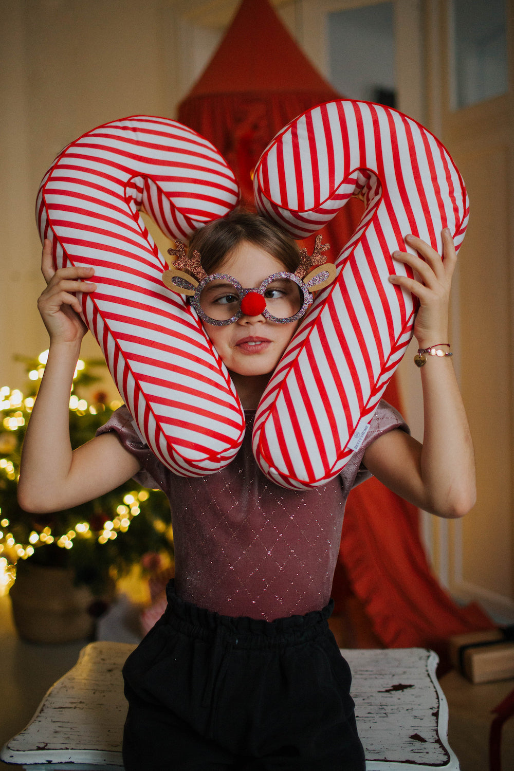 Christmas candy cane cushion red stripes by bettys home which is held by a girl by placing it on both sides of her head 