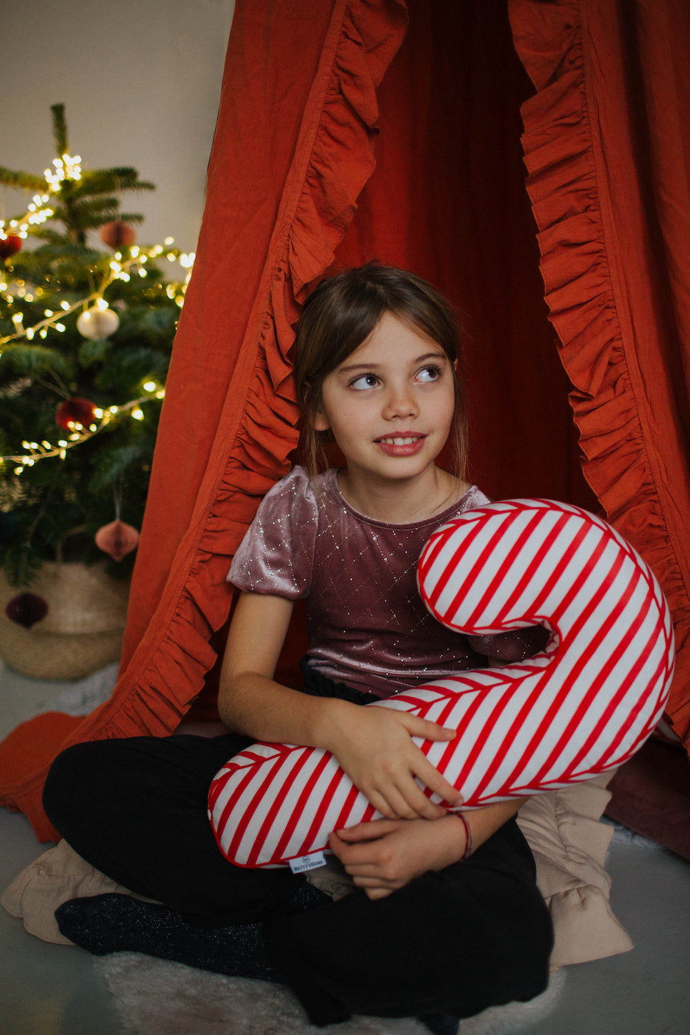 Christmas candy cane cushion red stripes by bettys home held by a little girl on her lap. Candy Cane Pillow Pottery Barn