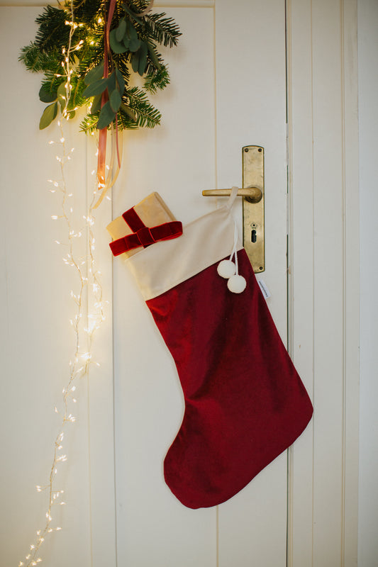 christmas stocking in wine red Hanging on a door handle with a small gift sticking out of the stocking by Bettys Home