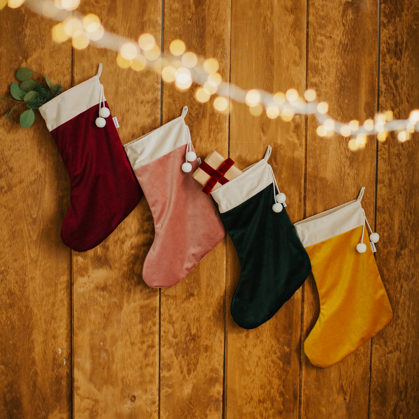 Four christmas stockings in velvet by bettys home with small gift inside hanging on wooden wall