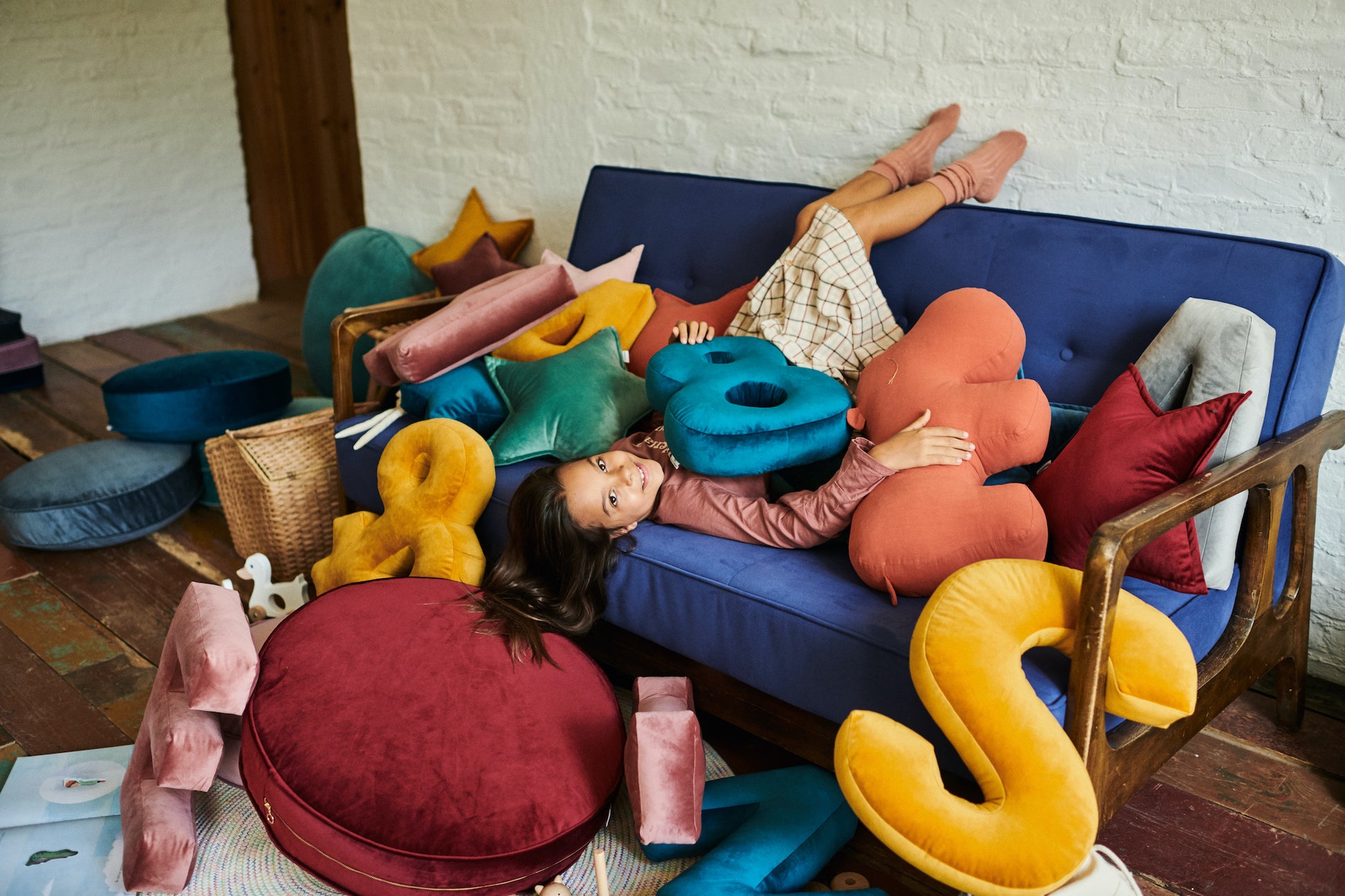 girl sitting on sofa with many velvet letter cushions and velvet star cushions by bettys home