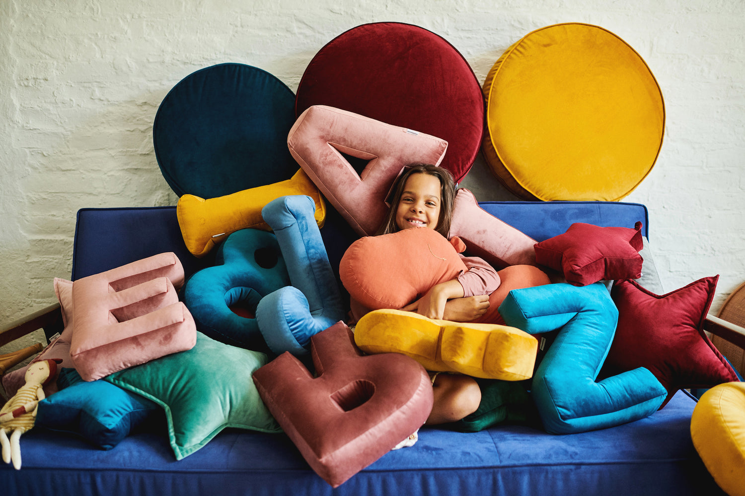 girl on sofa under many velvet letter cushions and large velvet poufs by betty's home
