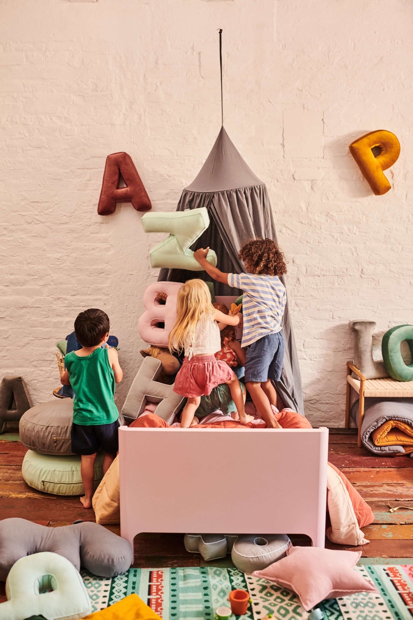 kids playing in kids room with velvet letter cushions. Over the bed is grey canopy by bettys home
