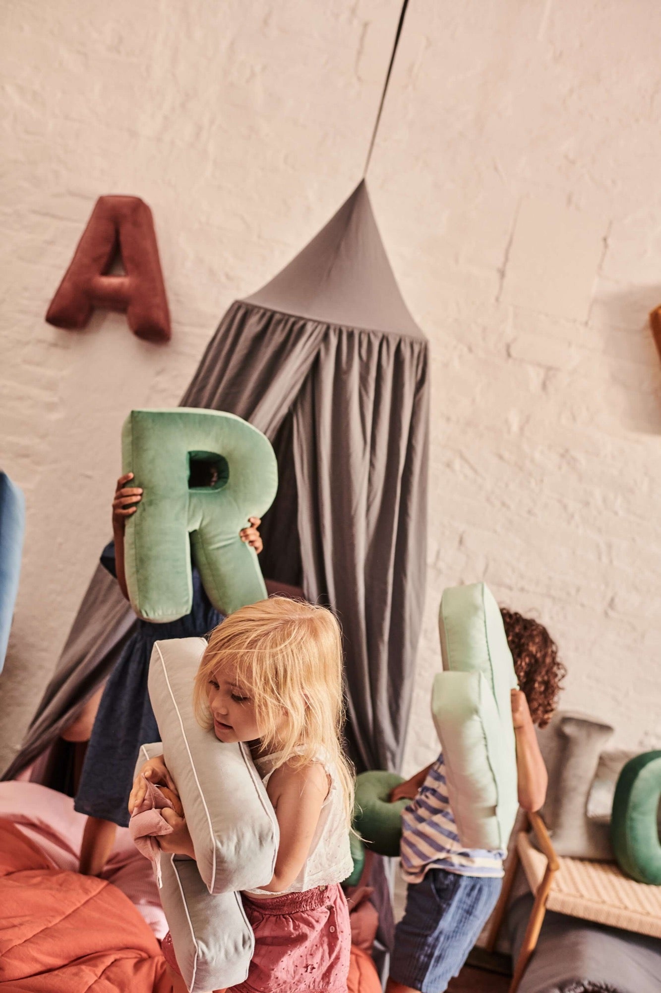 children playing in bedroom with velvet letter cushions uk by bettys home next to bed with cotton canopy
