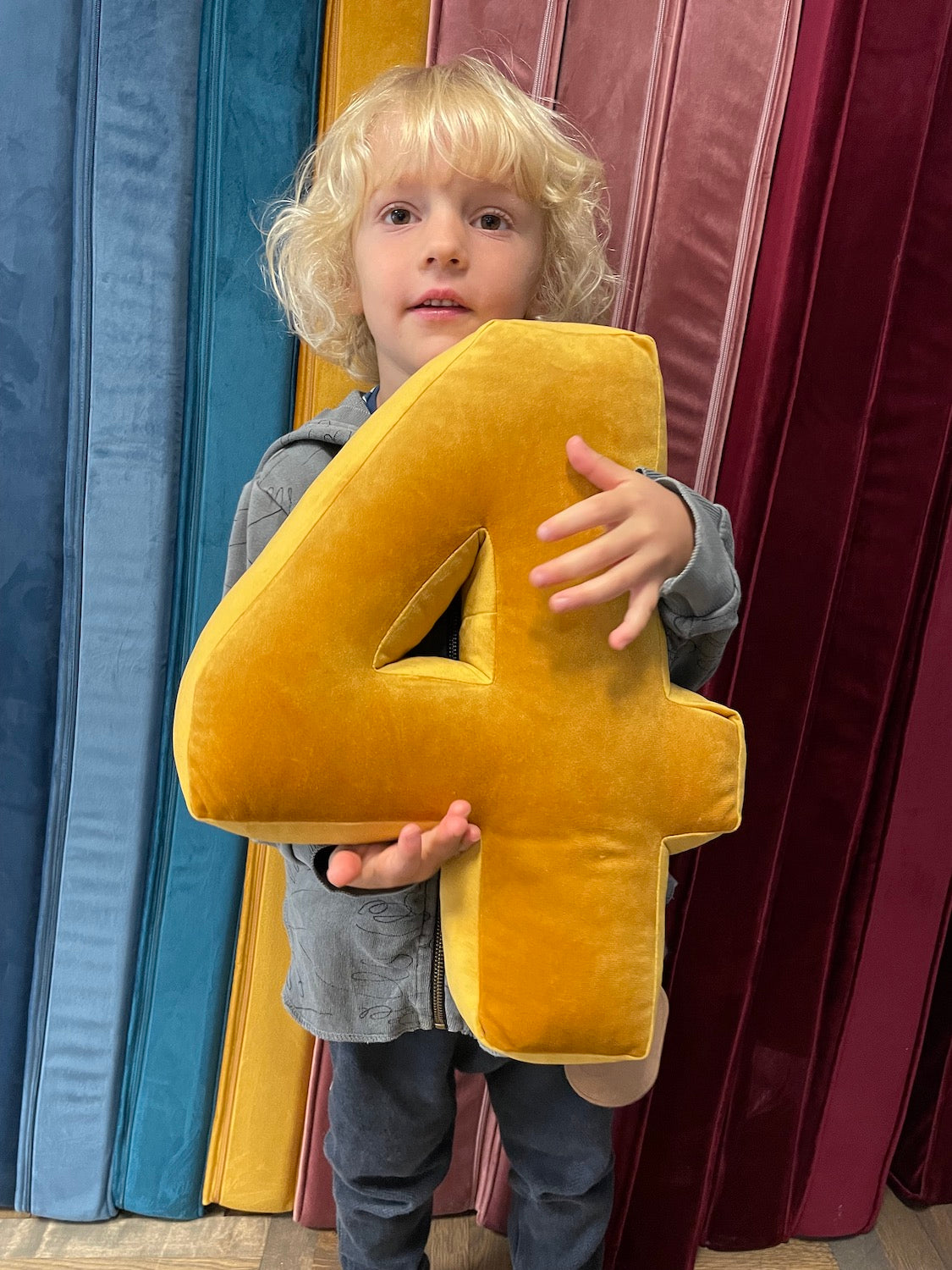 little boy holding velvet number cushion 4 in yellow by bettys home 