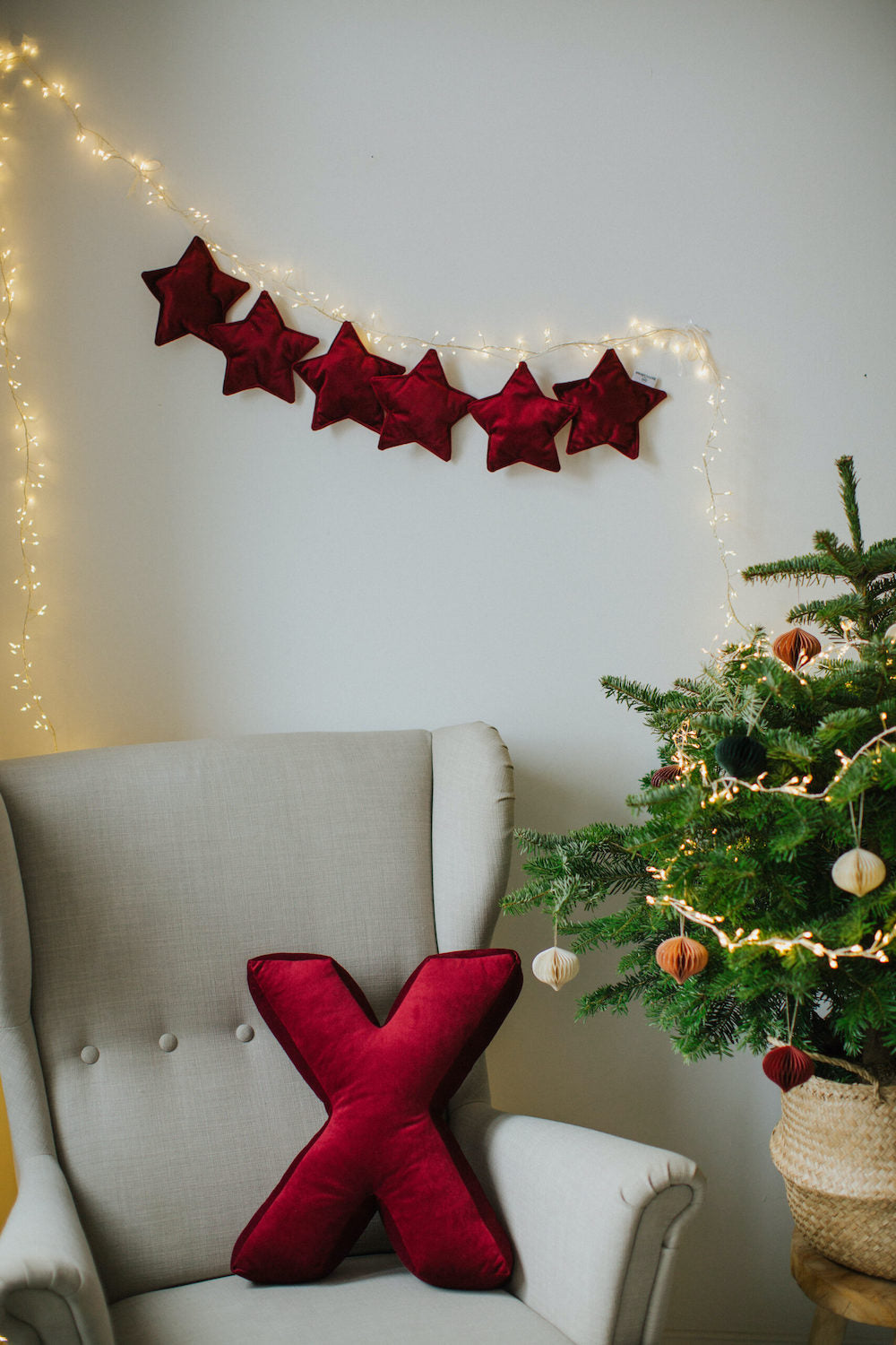 velvet star garland wine red on wall over armchair with velvet letter cushion X in wine near to Christmas tree