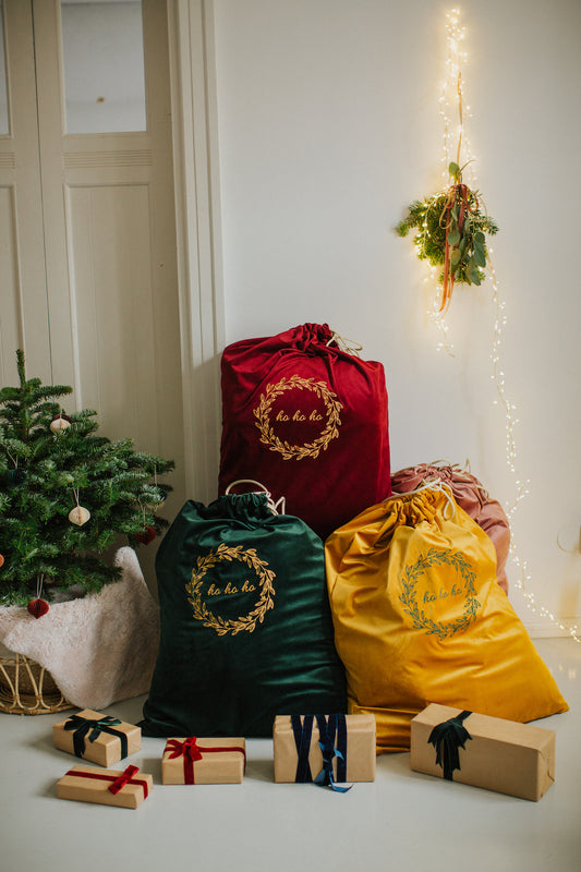 Three christmas gift sacks by Bettys Home with embroidered ho ho ho next to christmas tree and gifts